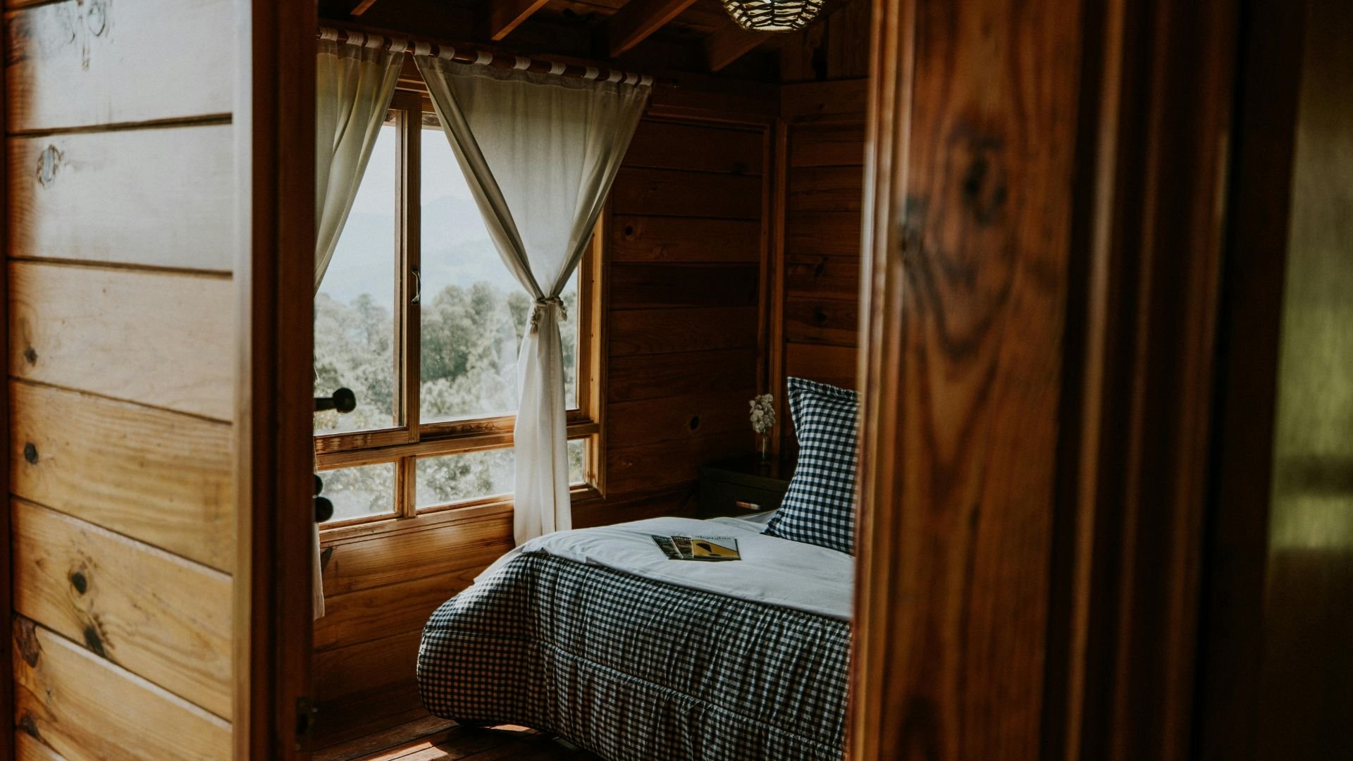 Cozy wooden cabin bedroom with gingham bedding and scenic window view