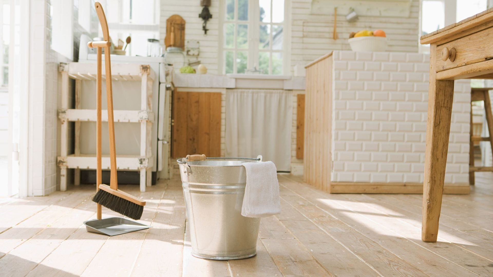Cleaning supplies with broom, dustpan, and bucket in bright wooden kitchen