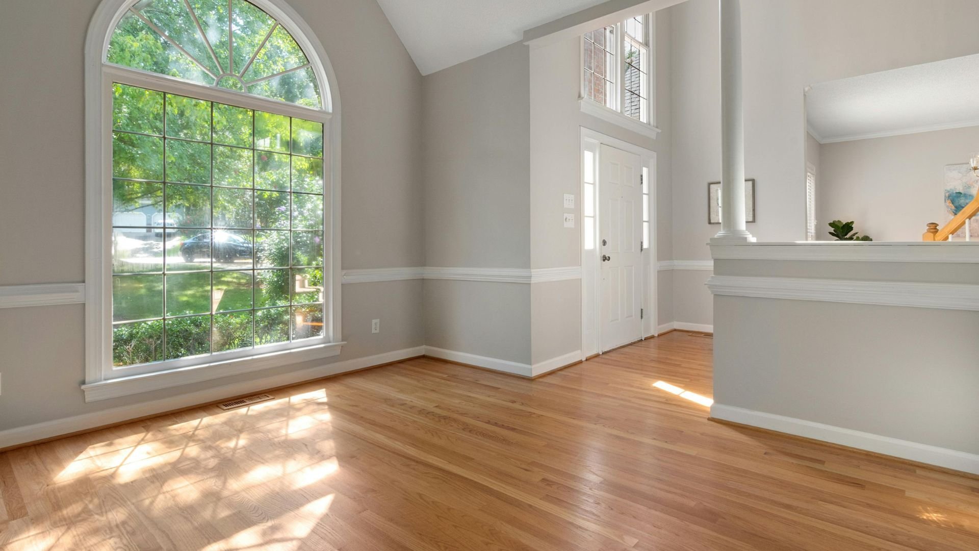Empty room with large arched window, hardwood floors, and natural light
